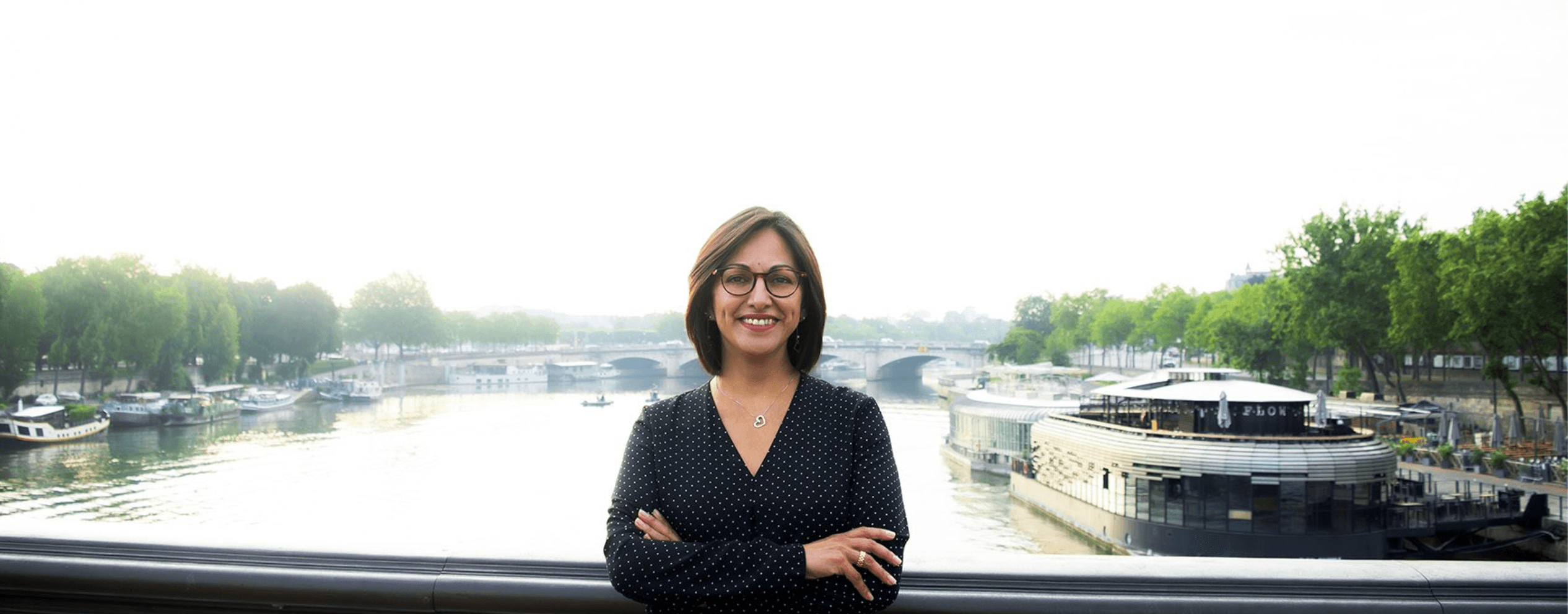 Ana Andón junto a un río, con un puente y arquitectura urbana al fondo.